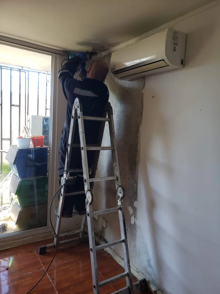 Técnico en escalera instalando un split en lo alto de un muro