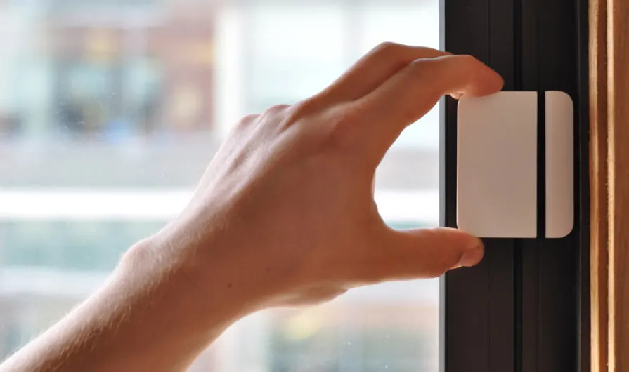 Mano instalando un sensor magnético en el marco de una puerta