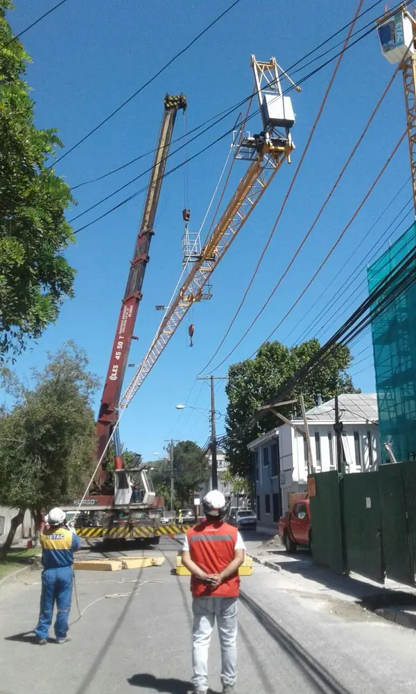 Camión grúa levantando un poste en una calle mientras dos técnicos supervisan
