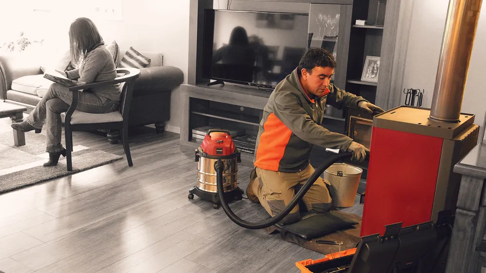 Técnico aspirando cenizas de una estufa en un living protegido