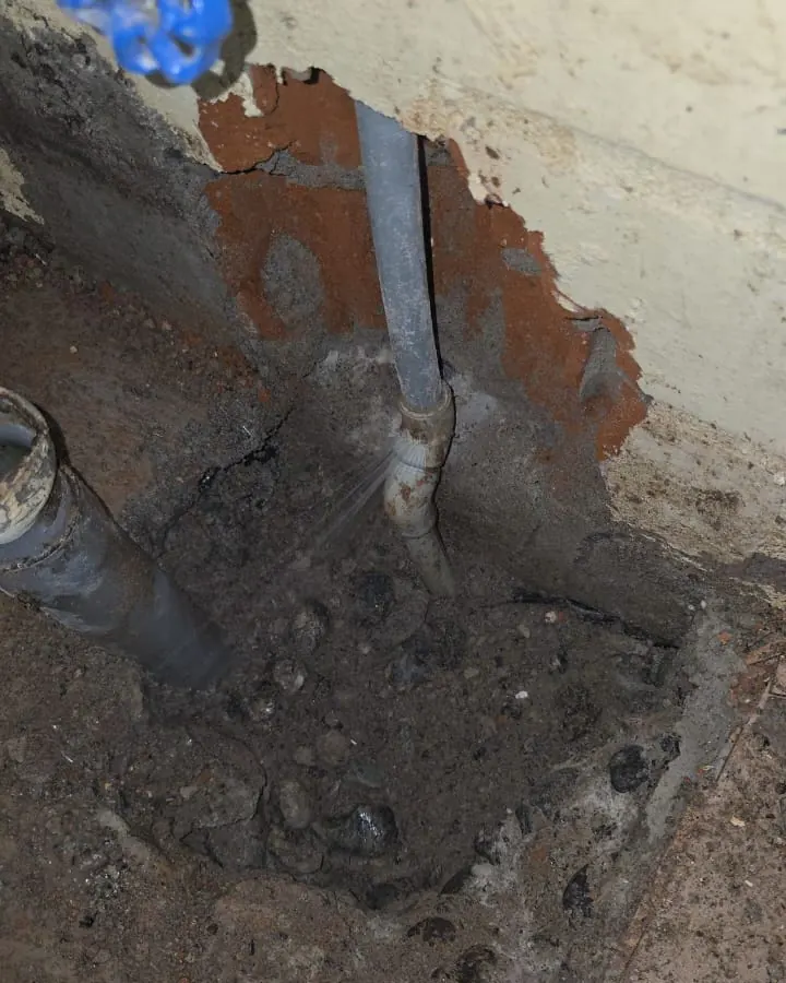Unión antigua bajo una llave de paso, con un chorro fino de agua saliendo de la cañería