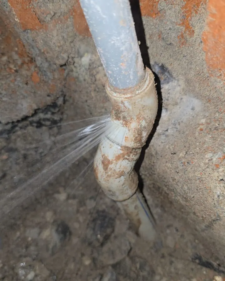 Chorro de agua saliendo de una unión antigua bajo una llave de paso