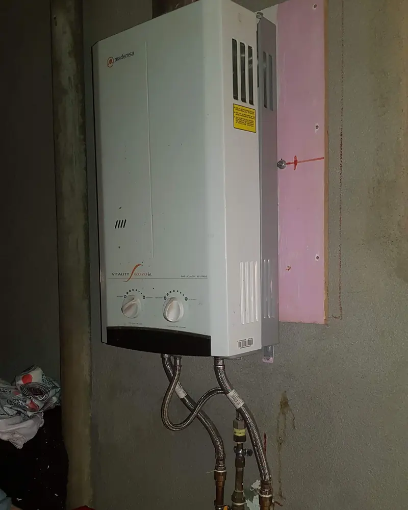 Calefont blanco instalado en el muro de una logia con sus conexiones