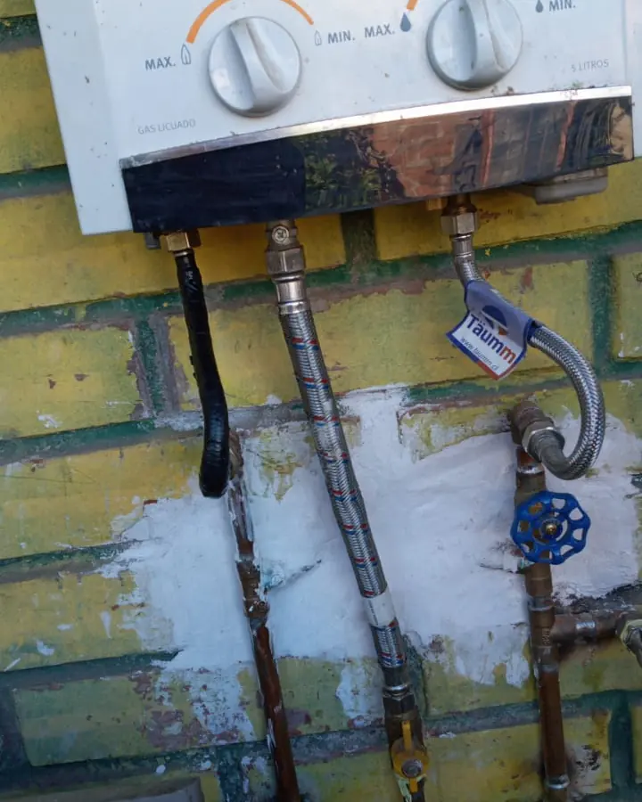 Calefont blanco en un muro de ladrillo con flexibles y llaves de paso