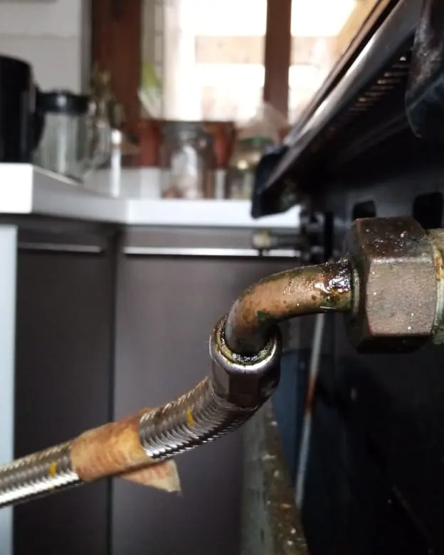 Conexión metálica oxidada de un flexible de gas detrás de una cocina