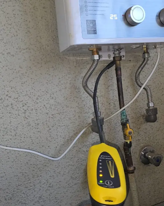 Detector de gas amarillo junto a las conexiones bajo un calefont