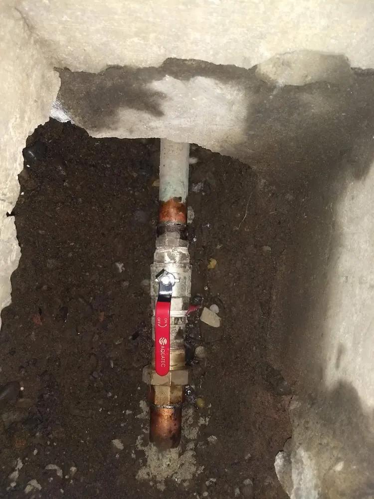 Llave de paso roja en una cañería bajo el piso excavado