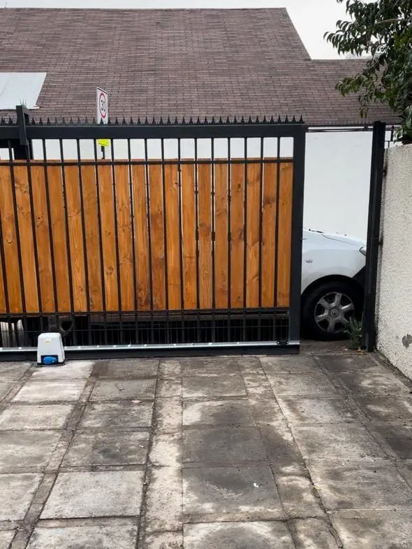 Portón de corredera de madera con luz destelladora frente a una casa